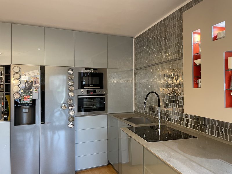 Küche mit grifflosen Fronten aus hinterlackiertem Glas und Fliesenspiegel in Edelstahl-Mosaik.