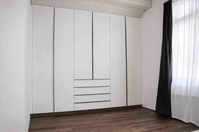Fertiger, grifflos gearbeiteter Einbauschrank an einer Dachschräge im bewohnten Raum, Boden und Fenster erkennbar.